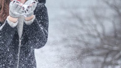 Winter - Woman in cozy winter clothing blowing snowflakes with excitement outdoors in a snowy setting.