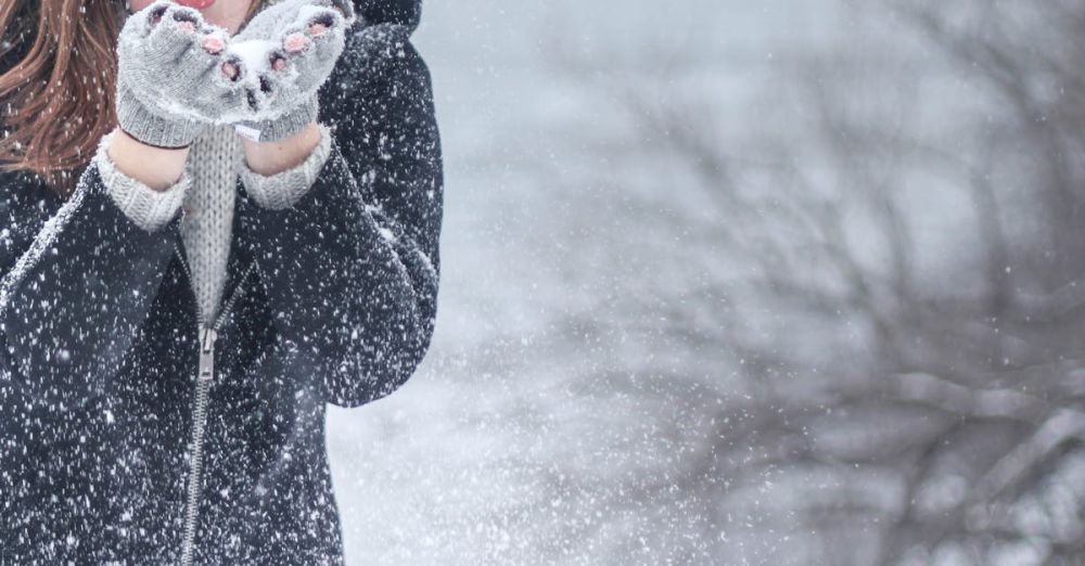 Winter - Woman in cozy winter clothing blowing snowflakes with excitement outdoors in a snowy setting.