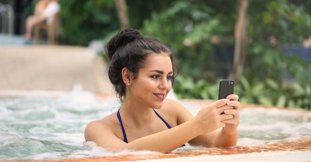 Hot Tubs - Smiling woman in a bikini enjoying a jacuzzi while texting on her smartphone outdoors.