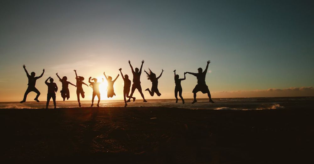 Groups - Silhouette of a group of friends jumping on a beach at sunset, expressing joy and freedom.