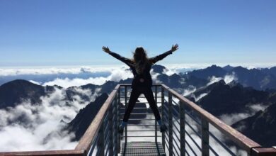 Adventures - A woman stands on a viewing platform in Vysoké Tatry, Slovakia, surrounded by clouds and mountains, embracing freedom.