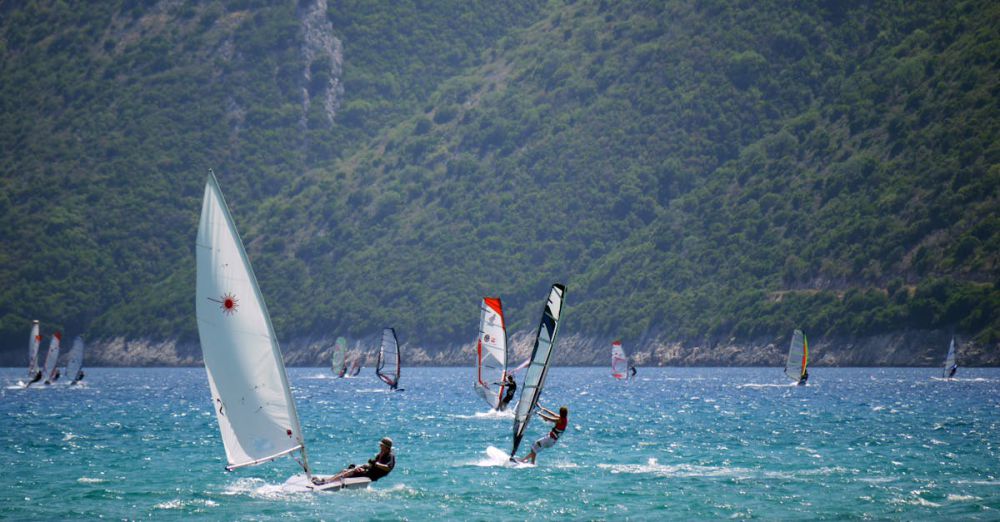 Windsurfing - Sailboats and windsurfers enjoy a sunny day on Vasiliki Bay, Greece with lush hills in the background.