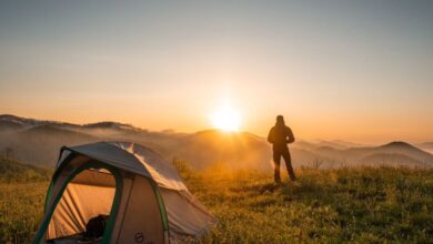 Camping - A camper enjoys the sunrise in a mountain setting with a tent. Perfect nature escape.