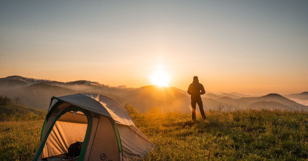 Camping - A camper enjoys the sunrise in a mountain setting with a tent. Perfect nature escape.