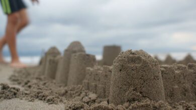 Sandcastle - Detailed shot of a sandcastle with a blurred figure on a cloudy beach day.