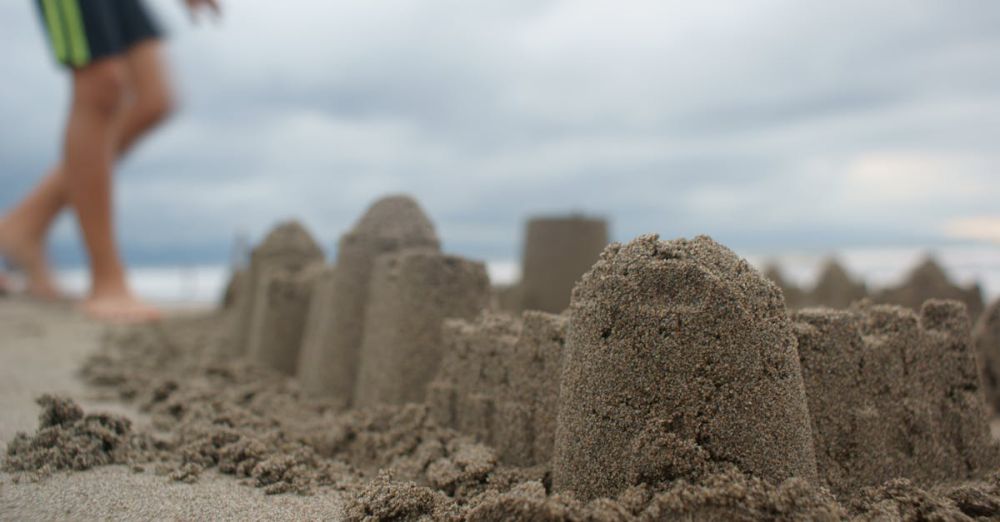 Sandcastle - Detailed shot of a sandcastle with a blurred figure on a cloudy beach day.