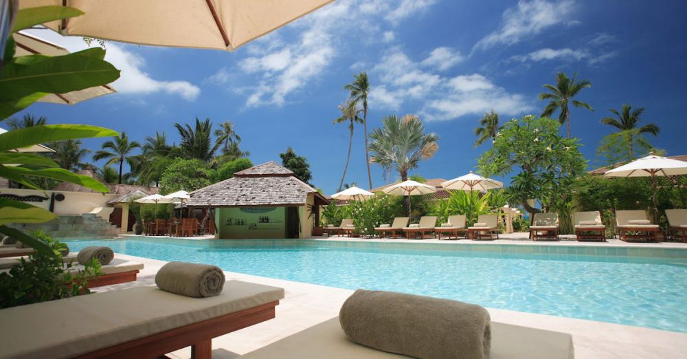 Resorts - Experience ultimate relaxation at a sunlit tropical poolside resort featuring palm trees and blue skies.