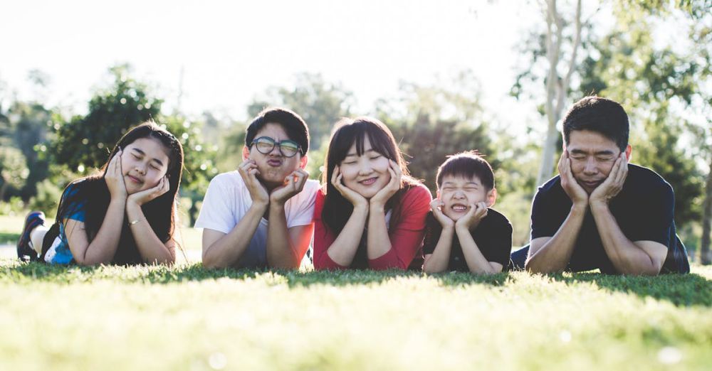 Family - Asian family posing happily on the grass in a sunny park, showcasing love and togetherness.