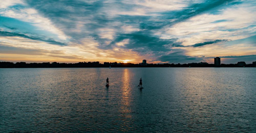 Paddleboarding - Tranquil sunset view of two people paddleboarding on a calm lake with dramatic clouds.