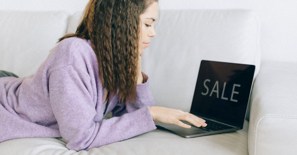 Fashion Deals - Woman browsing online sale while lying on a couch with shopping bags nearby.