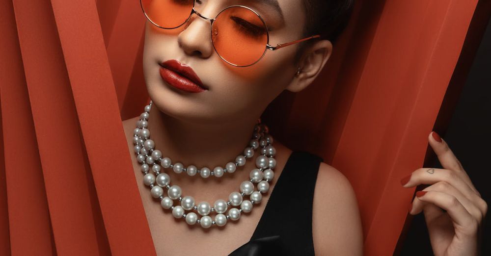 Luxury Fashion - Stylish woman in black dress, pearls, and orange sunglasses posing gracefully.