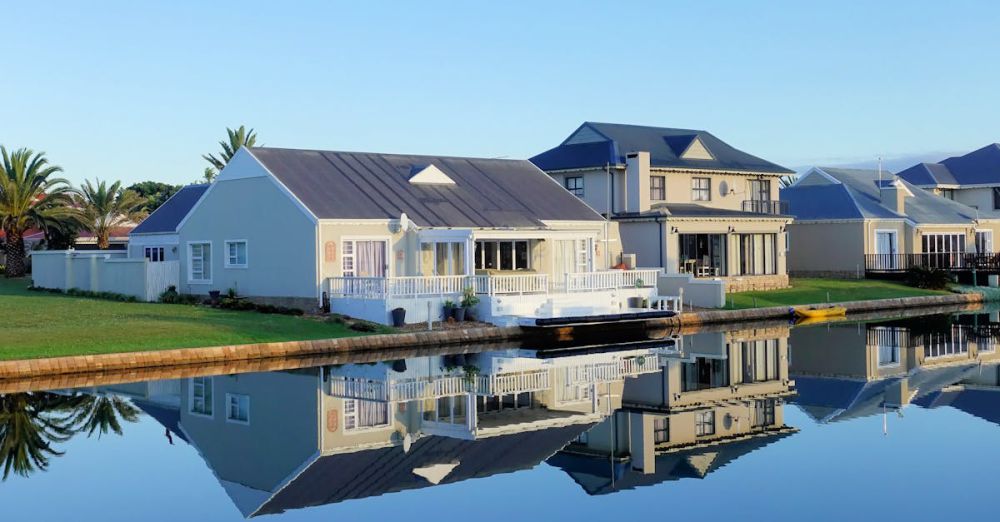 Luxury Property - Luxury modern homes reflecting on a peaceful, clear lake during daylight, showcasing architectural beauty.