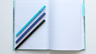 Pens - Open lined notebook with colorful pens on a white surface, perfect for note-taking and office tasks.