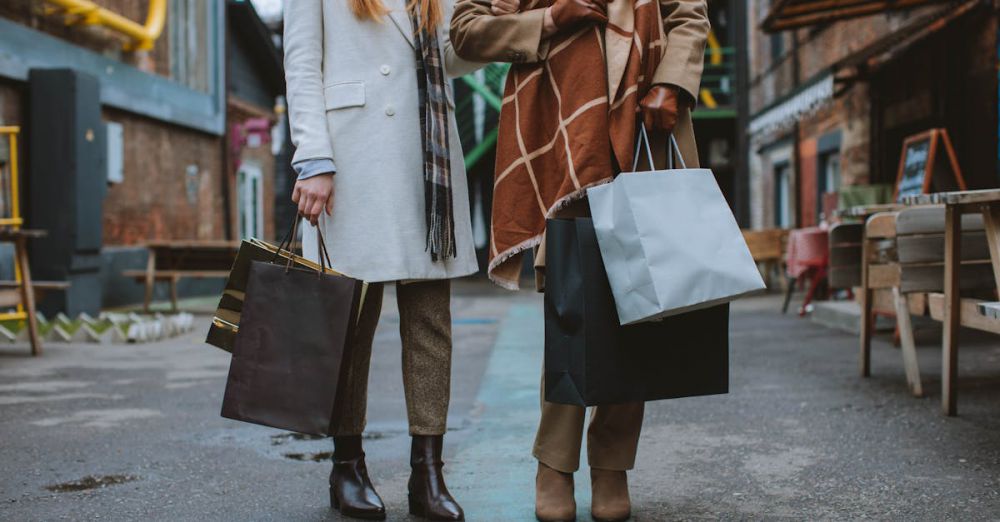 Black Friday - Two fashionable women walking and shopping on a city street with bags, wearing coats and boots in a winter setting.