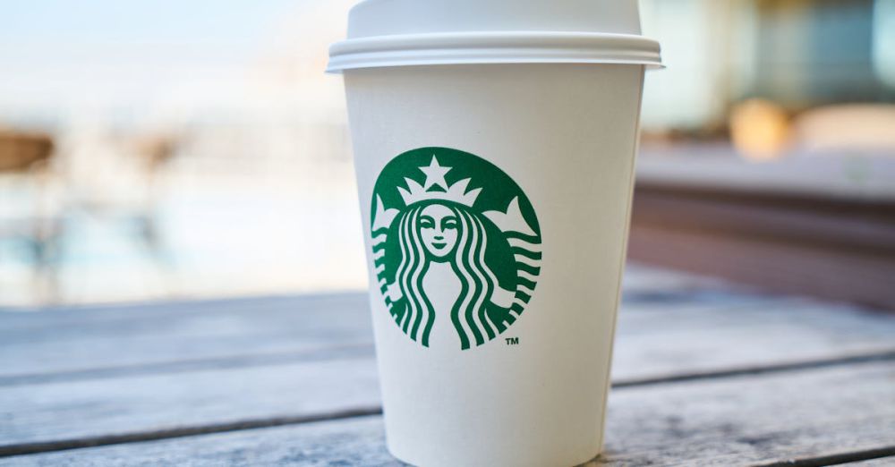 Brands - A disposable coffee cup with a lid outdoors on a wooden table, featuring a popular global logo.