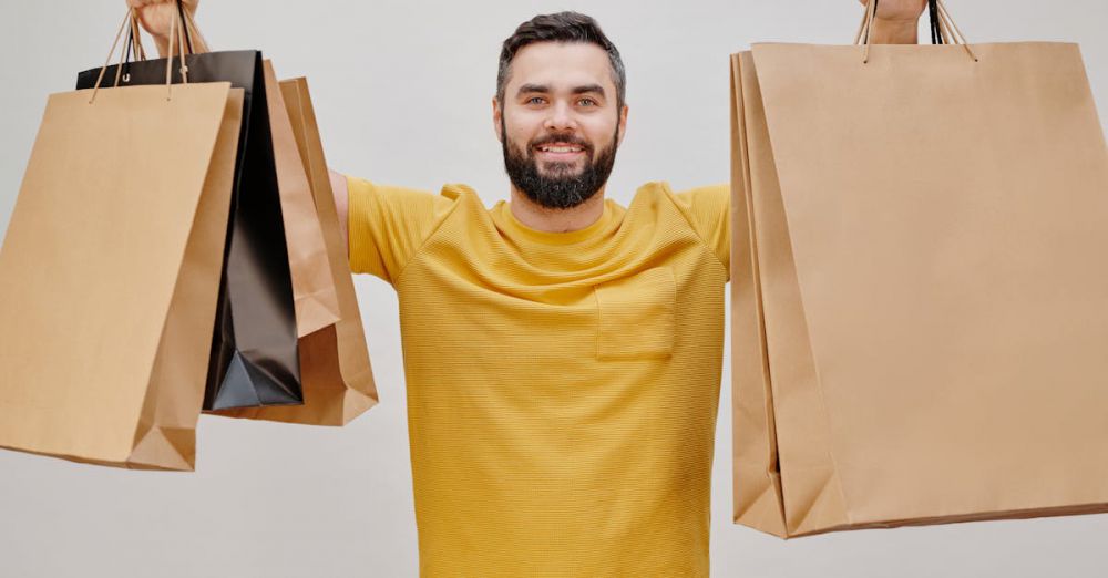 Coupons - Happy man in yellow shirt holding multiple shopping bags, expressing joy of shopping.