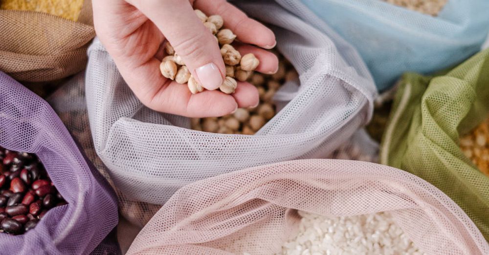 Bulk Buying - Hand holding chickpeas above colorful reusable bags with grains, promoting zero waste living.