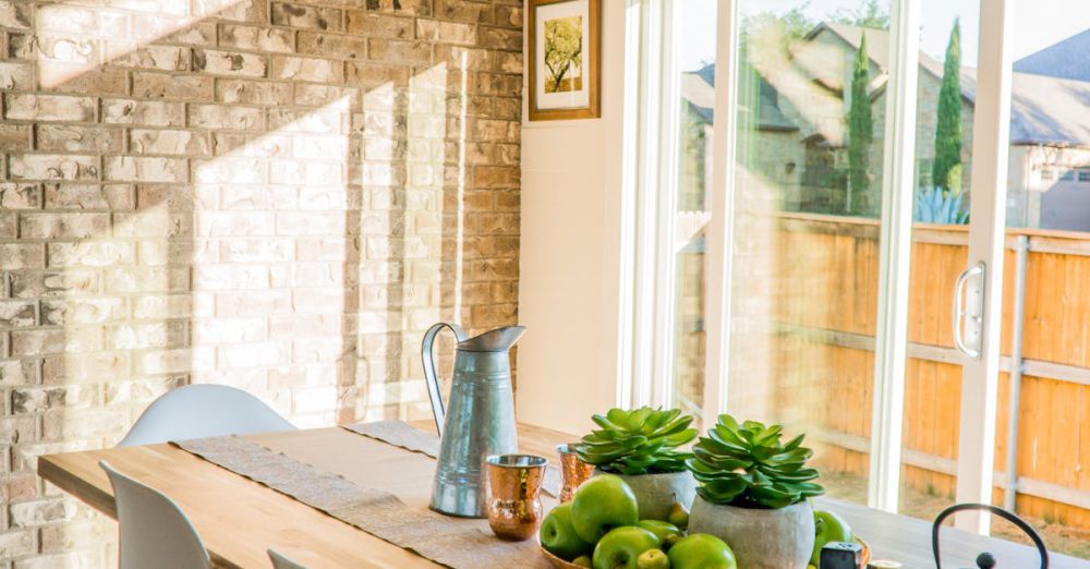 Home Decor - Sunlit dining room with contemporary decor and a rustic brick wall, featuring stylish lighting and a wooden table.