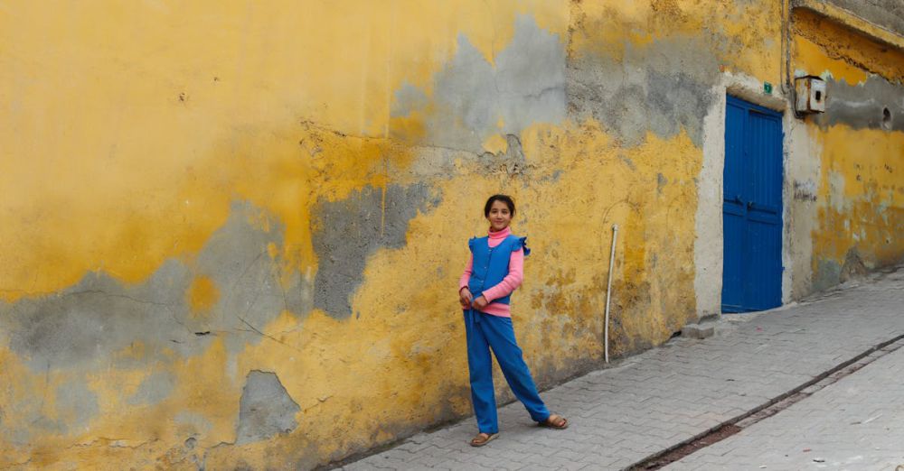 Kids’ Clothing - A young girl poses in front of a colorful textured wall on the streets of Şanlıurfa, Türkiye.