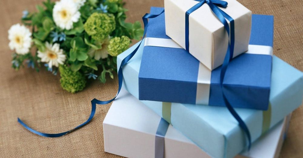 Gifts - Three beautifully wrapped gift boxes with blue ribbons arranged beside a floral bouquet.