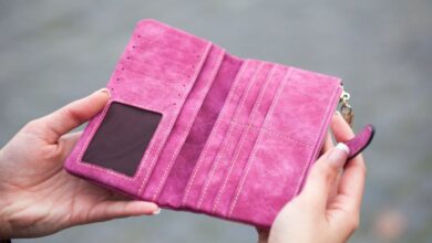 Wallets - A woman holds an open, empty pink wallet outdoors, emphasizing financial themes.