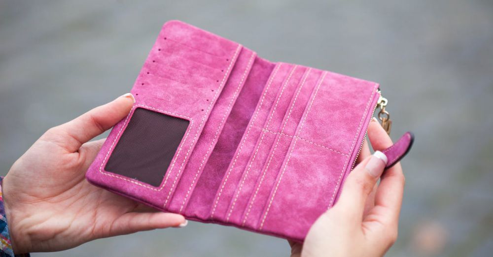 Wallets - A woman holds an open, empty pink wallet outdoors, emphasizing financial themes.