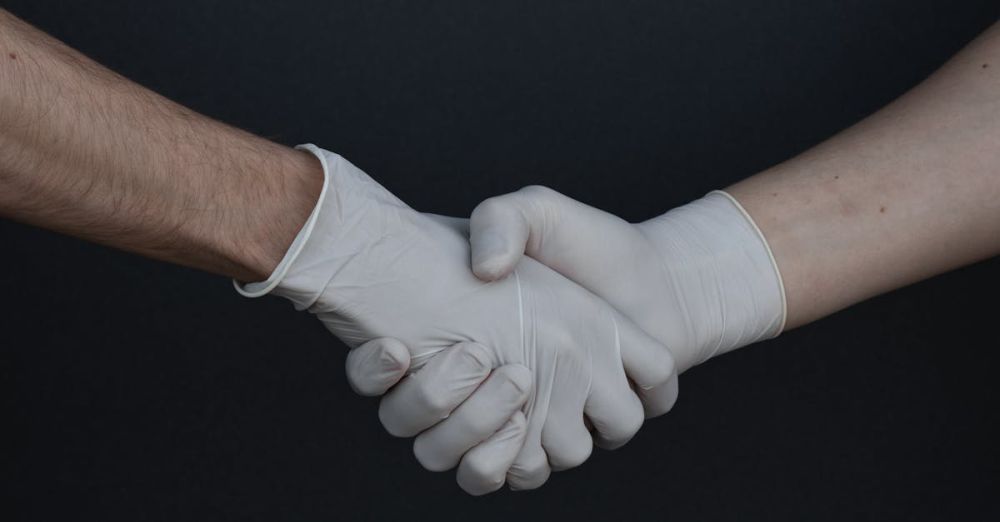 Gloves - Two people shaking hands while wearing latex gloves, illustrating safety and protection.