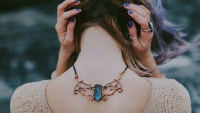 Necklaces - Glamorous young woman displaying a stylish gemstone necklace outdoors, posing with hands on head.