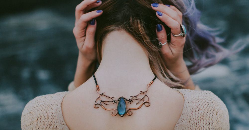 Necklaces - Glamorous young woman displaying a stylish gemstone necklace outdoors, posing with hands on head.