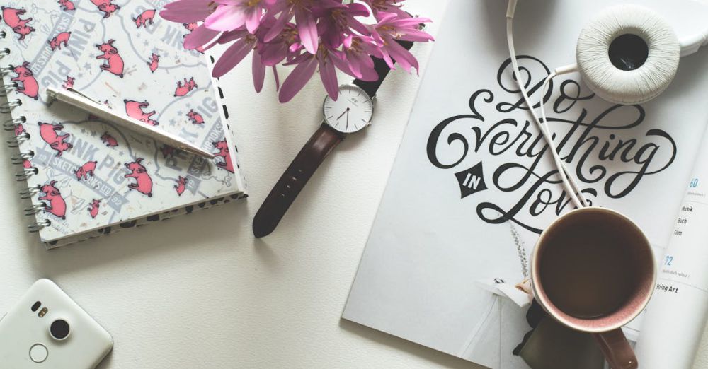 Accessories - Artistic flat lay featuring a workspace with a pink-themed notebook, flowers, and headphones.