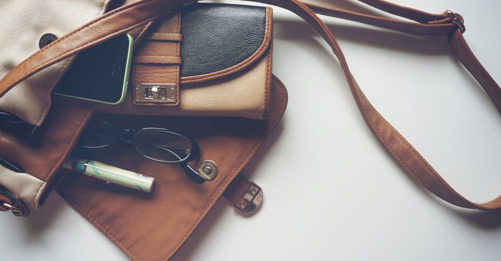 Wallets - Overhead view of leather bag with eyeglasses, wallet, and smartphone laid out.