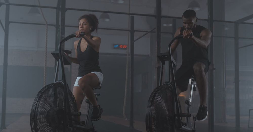 Exercise Bikes - A focused pair of athletes exercising on air bikes, showcasing endurance and fitness in a gym setting.