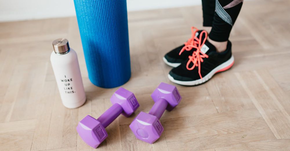 Gym Accessories - A pair of sneakers, purple dumbbells, yoga mat and bottle on wooden floor.