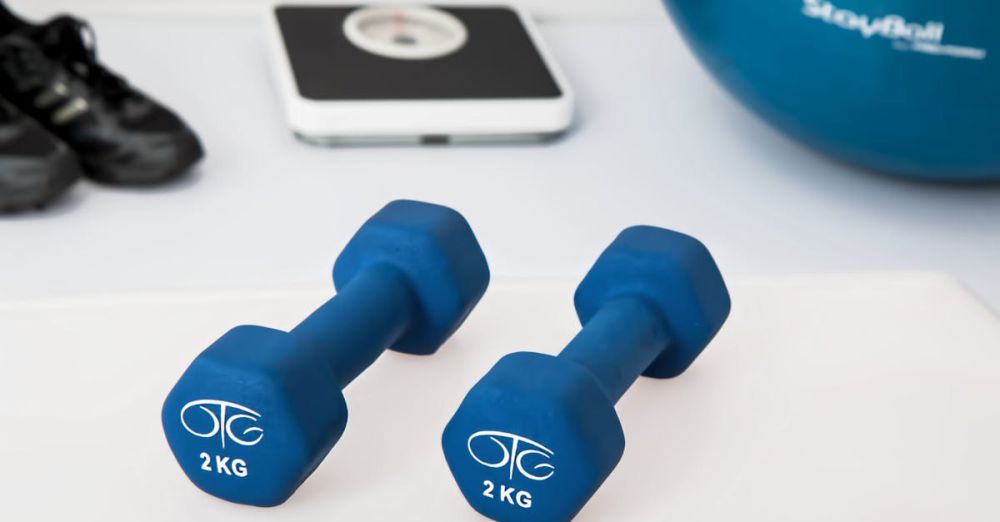 Exercise Equipment - Blue dumbbells placed on a white surface with fitness equipment in the background.