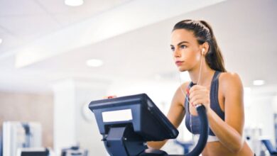 Ellipticals - Serious fit woman in earphones and activewear listening to music and running on treadmill in light contemporary sports center