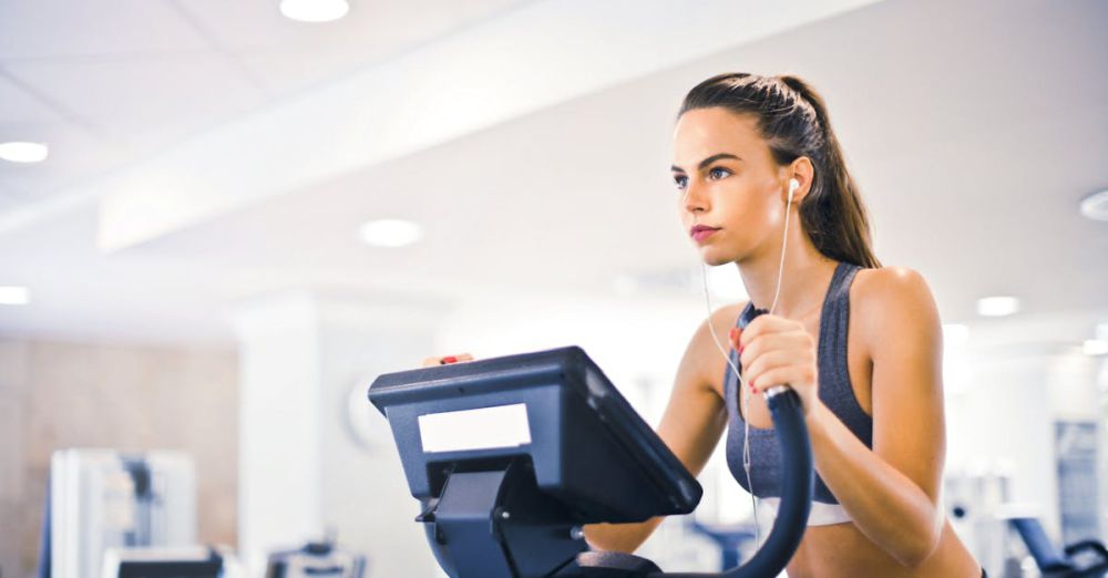 Ellipticals - Serious fit woman in earphones and activewear listening to music and running on treadmill in light contemporary sports center