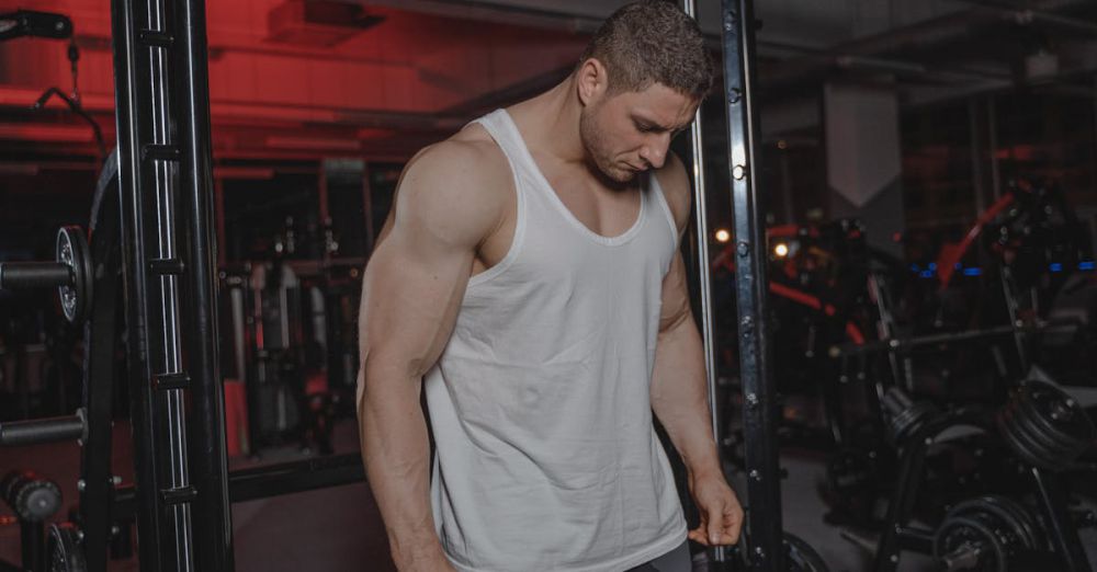 Treadmills - A muscular man in a gym wearing a white tank top, surrounded by weightlifting equipment.