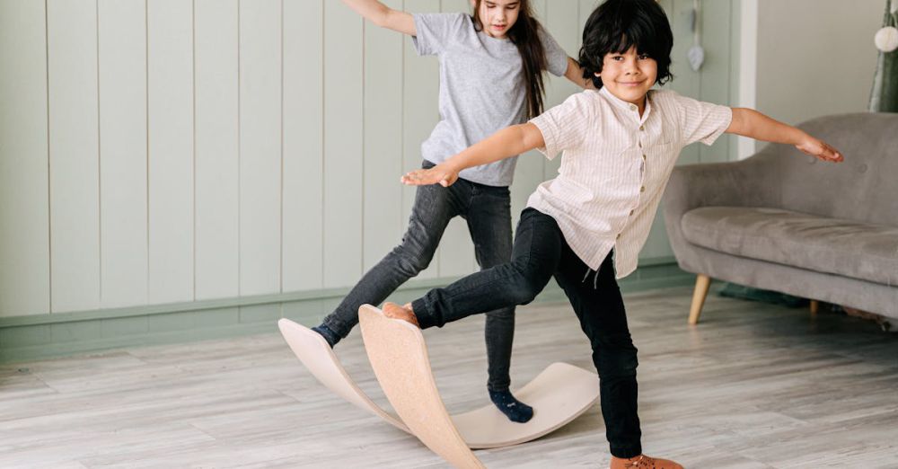 Balance Boards - Two children playfully balancing on curved wooden boards in a cozy indoor setting.