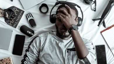 Gadgets - A young man lying on a bed surrounded by modern gadgets, books, and tech devices, illustrating digital lifestyle.