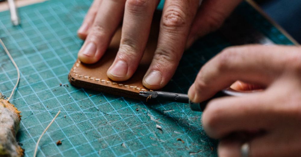 Tools - Hands working with leather and tools on a green cutting mat in a workshop setting.