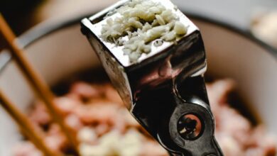 Garlic Press - Freshly pressed garlic in a stainless steel press with a cooking background.