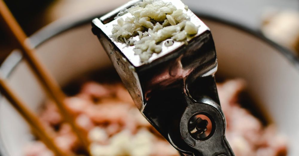 Garlic Press - Freshly pressed garlic in a stainless steel press with a cooking background.