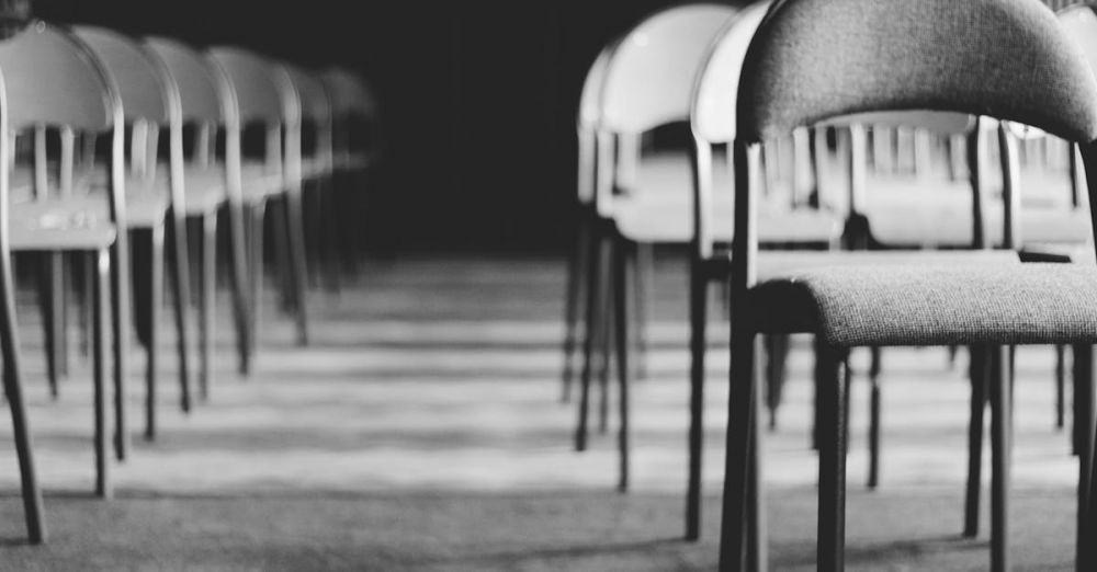 Chairs - Row of empty chairs in a dimly lit hall, captured in black and white.