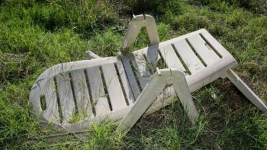 Patio Sets - An old, broken plastic lawn chair lying in overgrown grass outdoors.