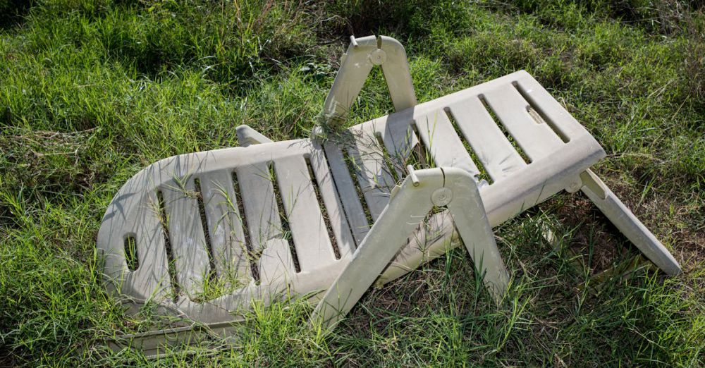 Patio Sets - An old, broken plastic lawn chair lying in overgrown grass outdoors.