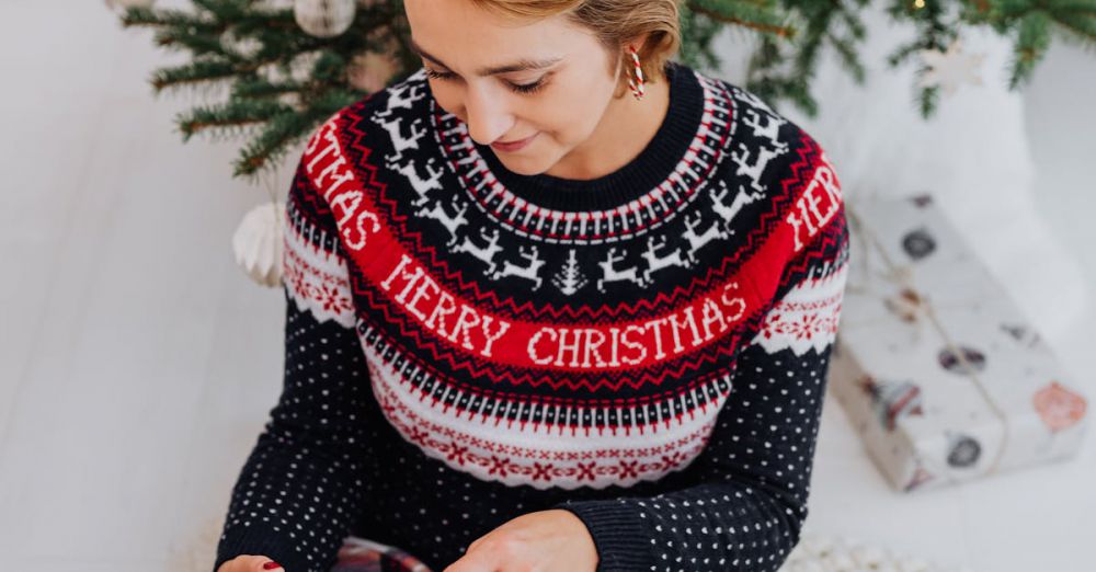 Gift - Woman in a festive sweater opens a gift beside a Christmas tree indoors.