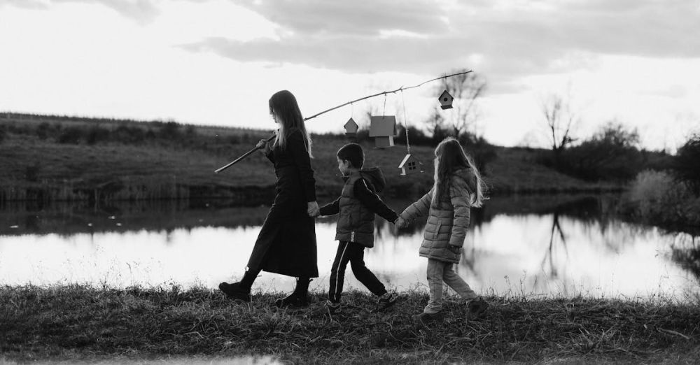 Birdhouses - A mother and children walk by a tranquil lake, carrying birdhouses on a stick, in black and white.