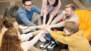 Bean Bags - A diverse group of adults sit indoors, joyfully stacking hands together, symbolizing teamwork and camaraderie.