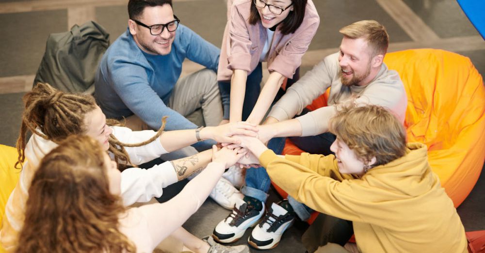 Bean Bags - A diverse group of adults sit indoors, joyfully stacking hands together, symbolizing teamwork and camaraderie.