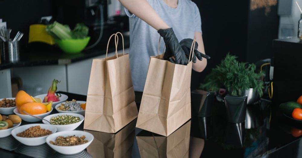 Meal Kits - A person in a kitchen packing food ingredients into paper bags for takeout orders.